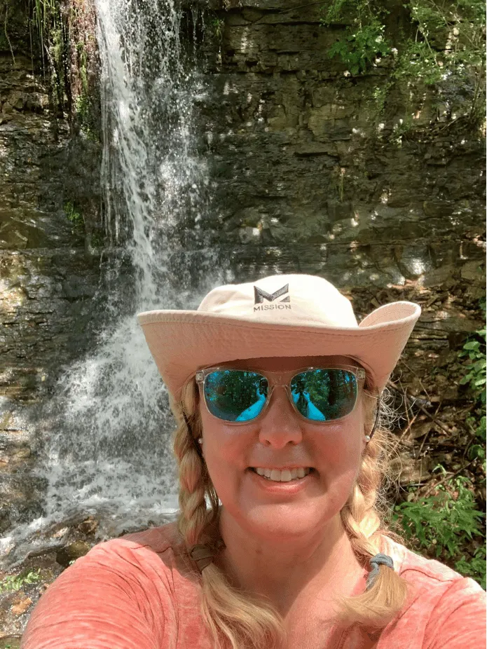 Sher standing in front of a waterfall wearing a big smile