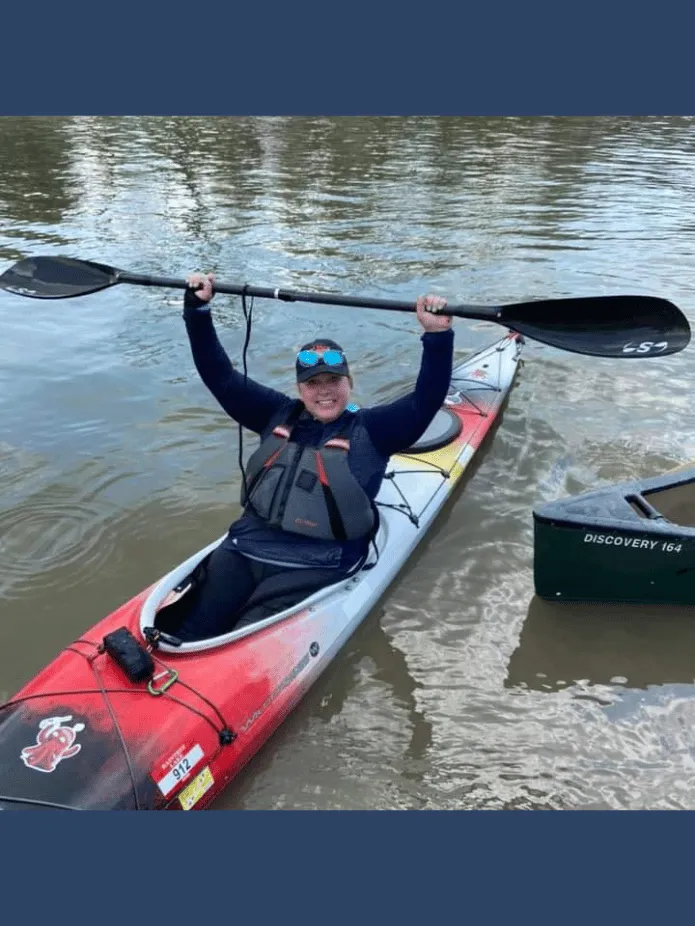 Sher in her kayak with the paddle held high above her head - victory paddle